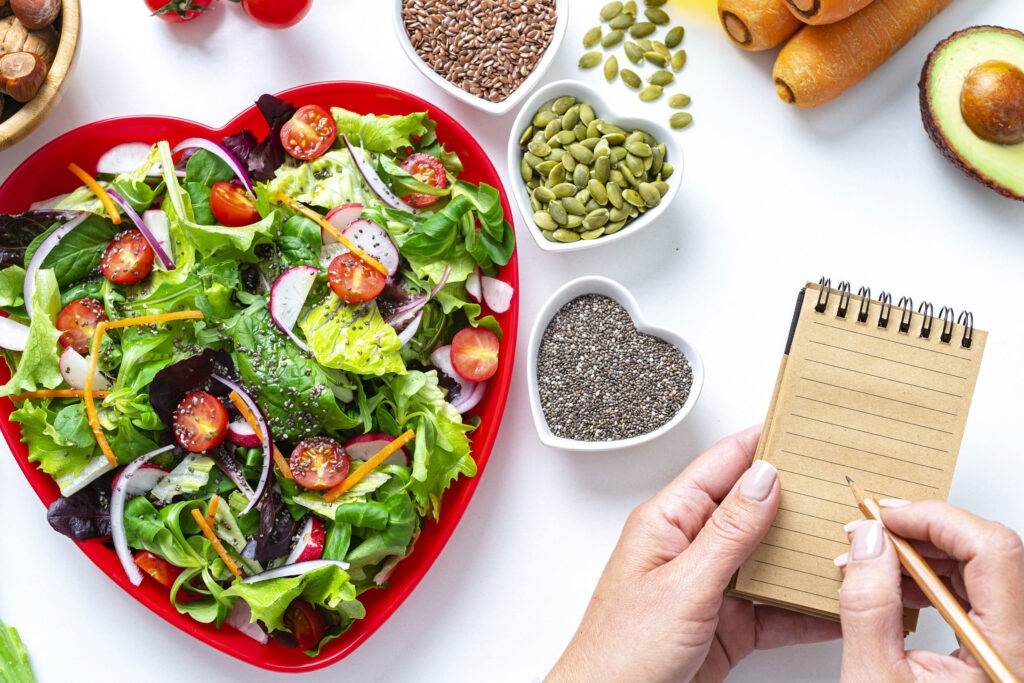 un plato de ensalada en forma de corazón junto a un bloc de notas