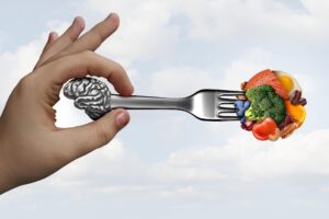 a hand holding a fork with a brain and vegetables on it