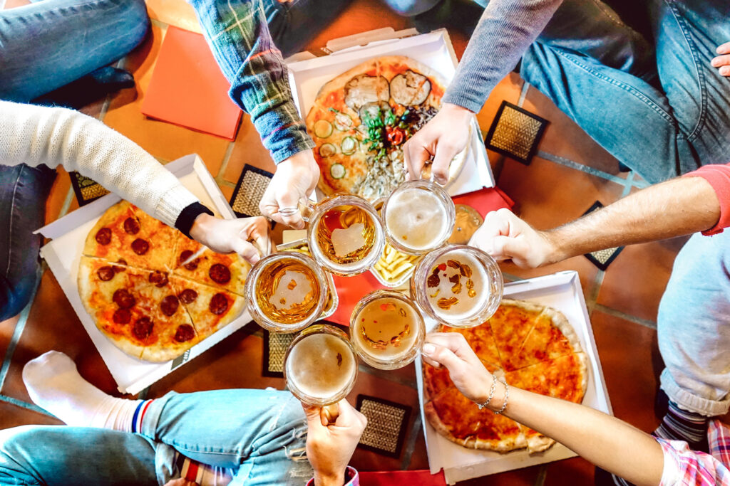 a group of people holding glasses of beer and pizza