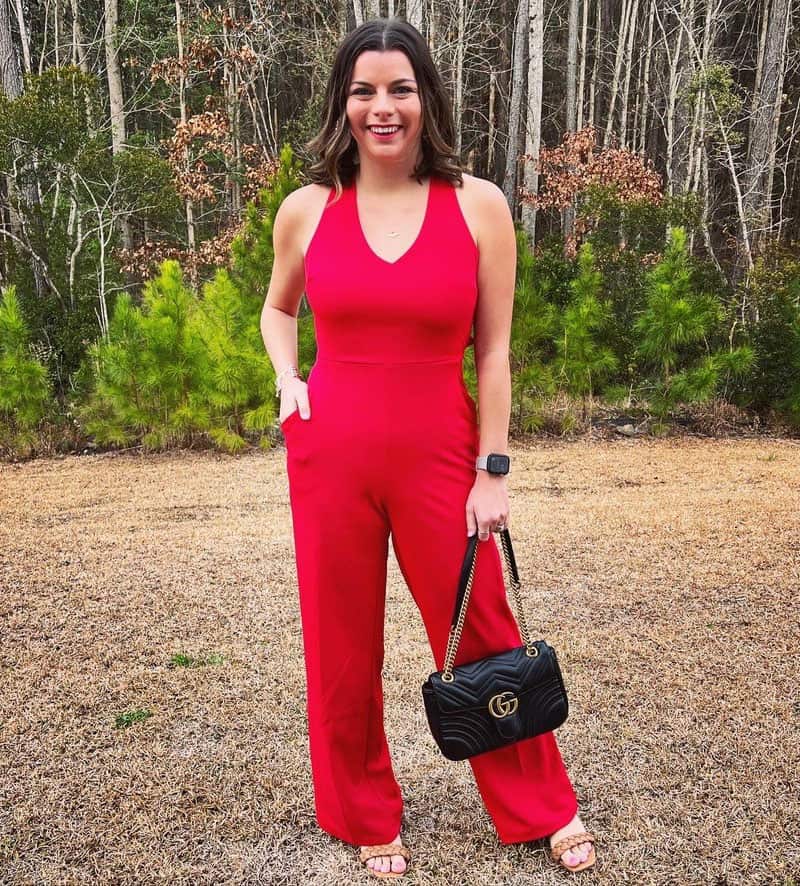 a woman in red jumpsuit standing in front of trees