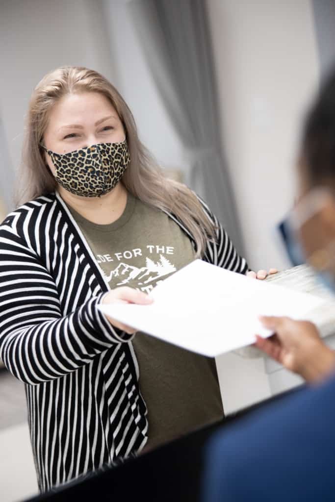 woman with mask over mouth handing over paperwork